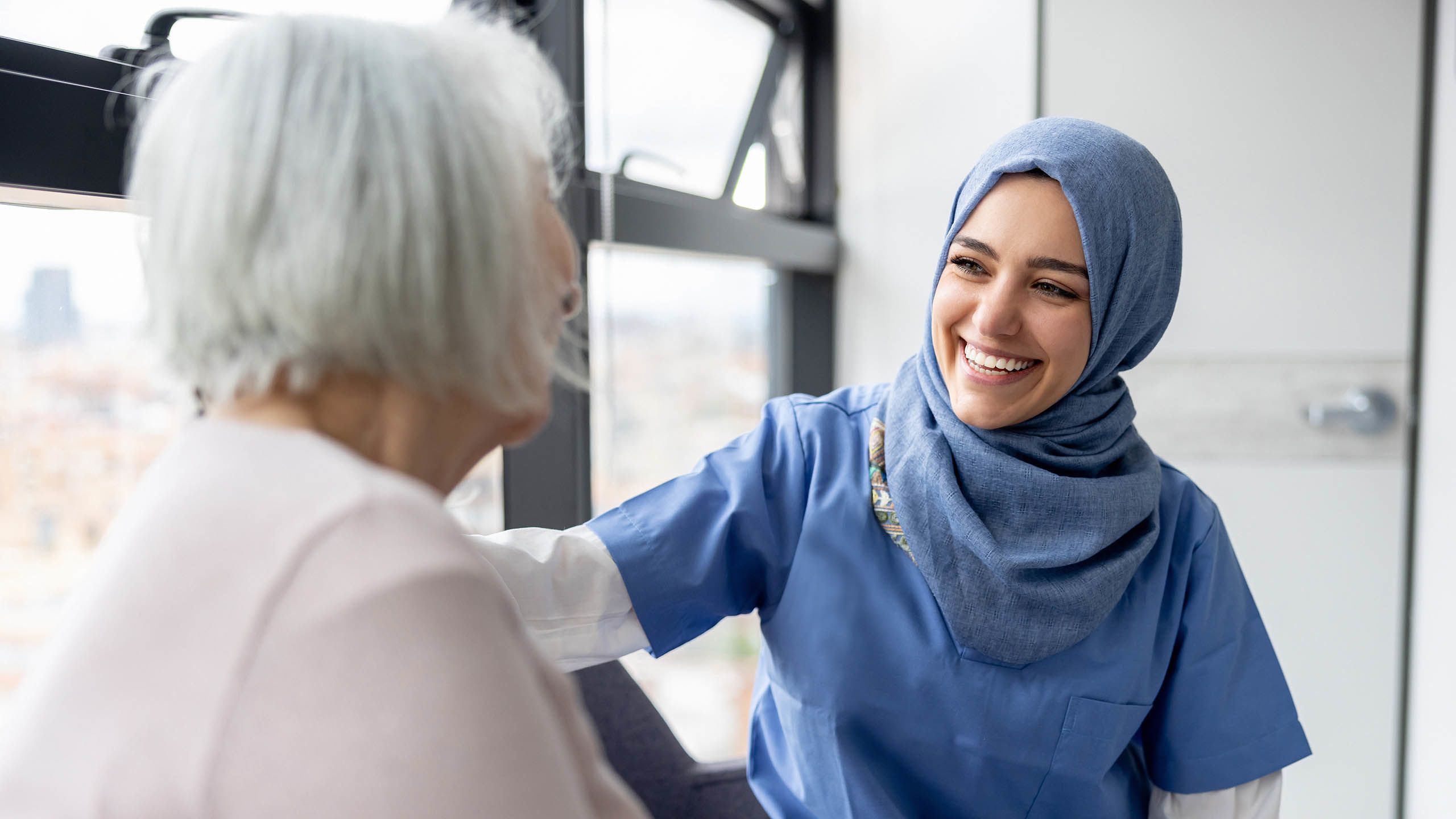 Photo depicting a Muslim nurse talking to a senior patient at the hospital and smiling  (andresr/E+ via Getty Images)